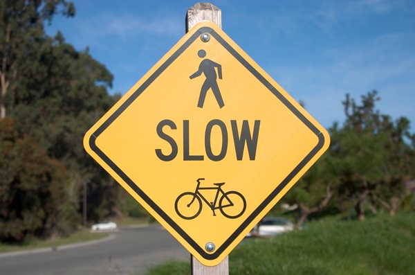 Yellow street sign with pedestrian and bicycle icons warning drivers to slow down. (149618)