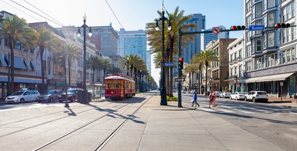 Streetcar traveling along Canal Street in New Orleans with palm trees, traffic, and pedestrians crossing. (763507930)